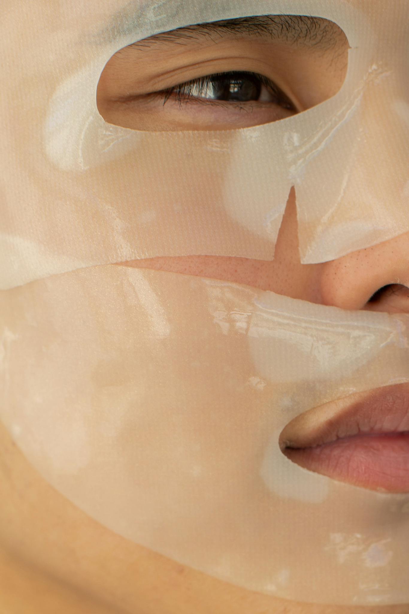 A close-up photo showing the application of a hydrating facial sheet mask on a person's face.